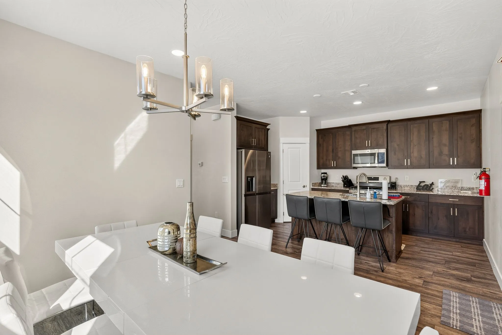Open-concept dining and kitchen area featuring a modern chandelier, dark wood-finish cabinetry, stainless steel appliances, a kitchen island with seating, and wood-finish flooring