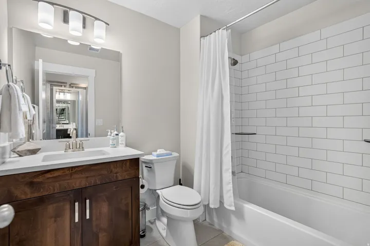 Bathroom featuring a white subway tile shower surround with integrated shelving, a white bathtub, and a wood-finish vanity with a white countertop and rectangular sink