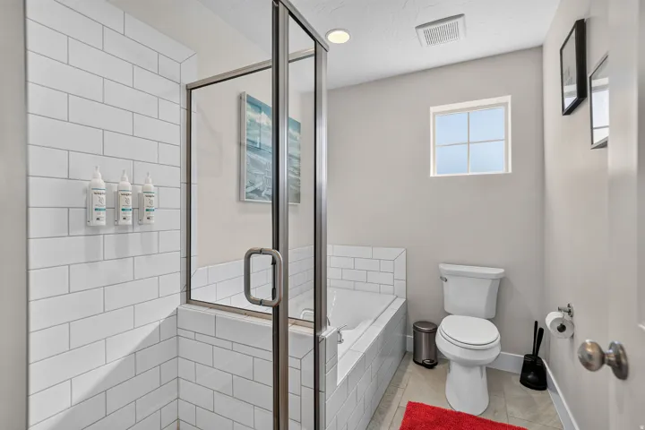 Full bathroom featuring a glass-enclosed shower, built-in soaking tub, subway tile surround, and a privacy window