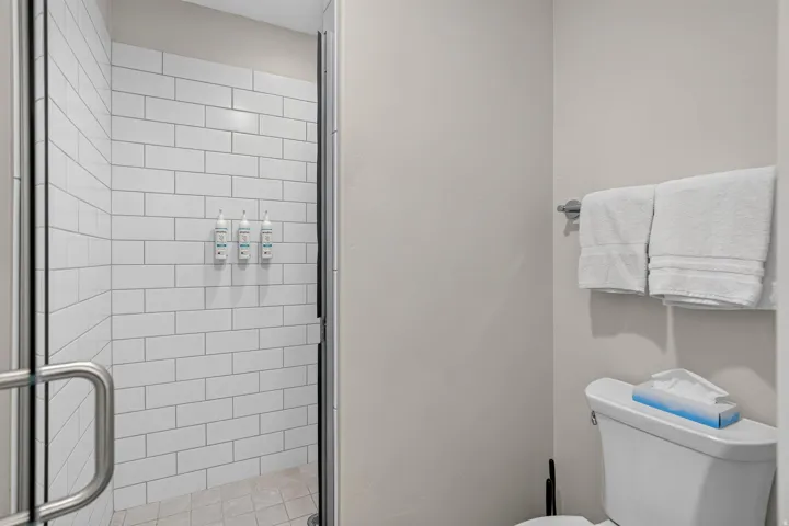 Walk-in shower featuring white subway tile, a clear glass enclosure, and a light-toned tile floor