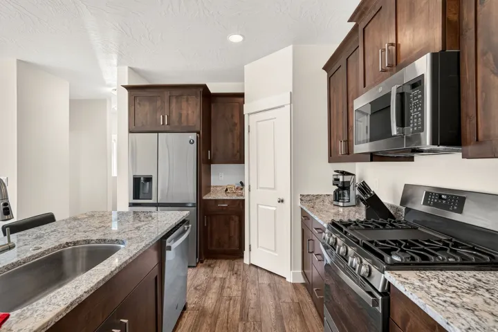 Modern kitchen featuring dark wood cabinetry, light granite countertops, stainless steel appliances, and wood-finish flooring