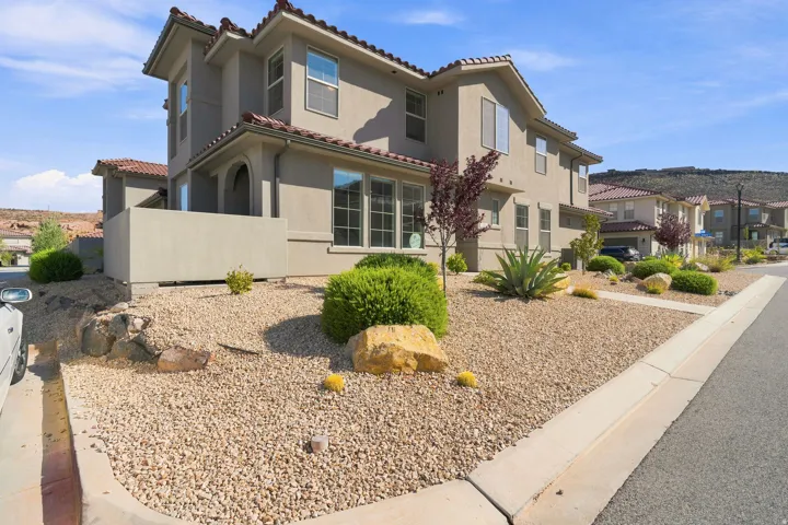 Stucco exterior with terracotta roof tiles, xeriscaped front yard with decorative gravel, and mature shrubbery