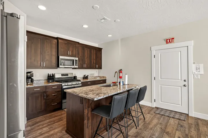 Kitchen featuring dark wood cabinetry, stainless steel appliances, a center island with bar seating, granite countertops, and wood-finish flooring