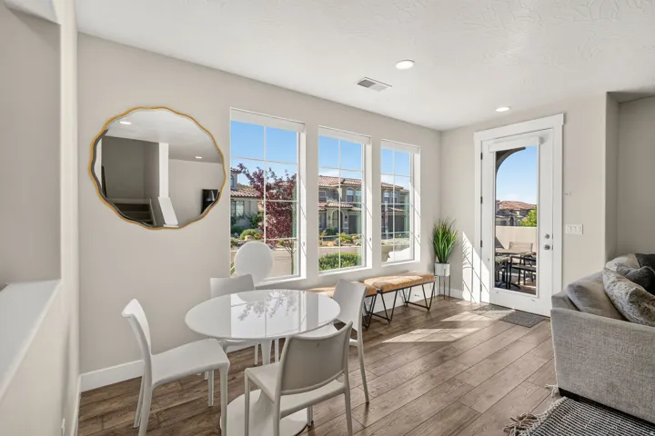 Bright living space featuring wood-finish flooring, three large windows, a glass-paneled door opening to an outdoor area, recessed ceiling lighting, and a neutral wall color