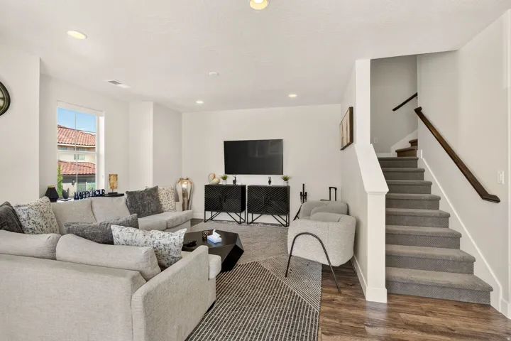 Living area featuring recessed lighting, a window with exterior views, wood-finish flooring, and a carpeted staircase with a dark wood handrail