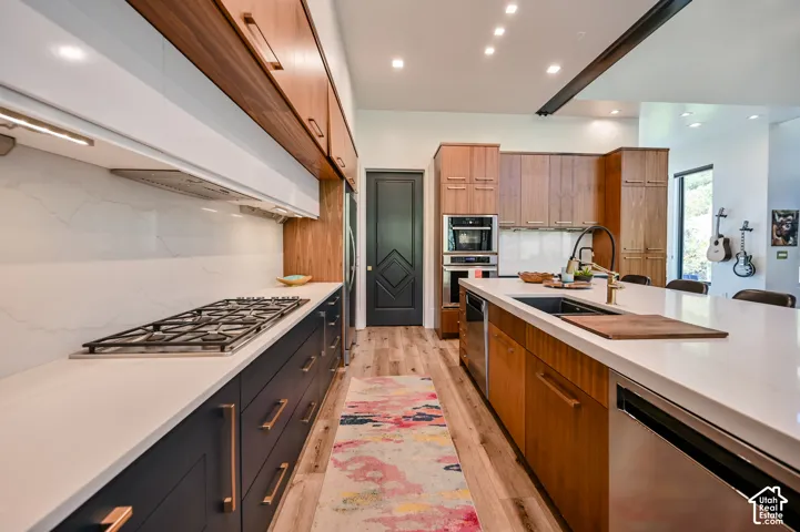 Modern kitchen featuring a gas range, white countertops, built-in stainless steel appliances, a kitchen island with an undermount sink, and wood-finish flooring