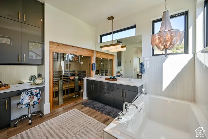 Contemporary bathroom featuring a built-in sauna with glass doors, a dual vanity with undermount sinks and quartz countertops, a large soaking tub with deck-mounted fixtures, and a vanity area with built-in cabinetry and a mirror