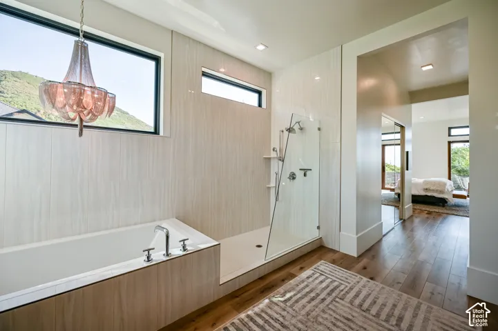 Freestanding soaking tub with chrome fixtures, glass-enclosed shower with multiple showerheads, and wood-finish flooring