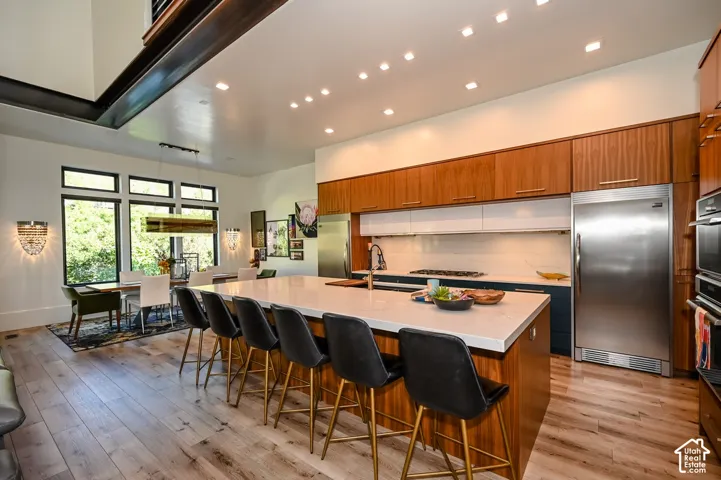 Open-concept kitchen and dining area featuring light wood-finish flooring, a kitchen island with seating, a gas range, and stainless steel appliances