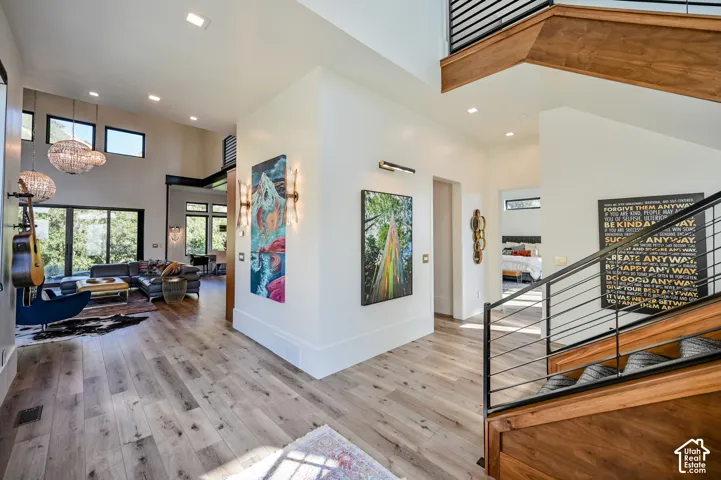 Expansive living area featuring light wood-finish flooring, a contemporary staircase with wood and metal railings, high ceilings, large windows, and recessed lighting