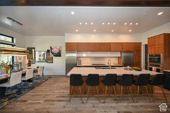 Gourmet kitchen featuring a large island with white stone countertop, built-in stainless steel appliances, wood-finish cabinetry, and wood-finish flooring