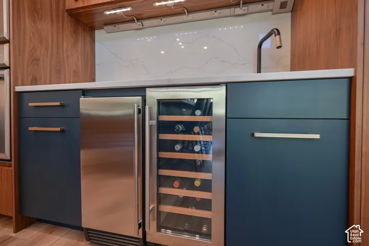 Wet bar featuring navy cabinetry, a stainless steel beverage refrigerator, and a built-in wine cooler