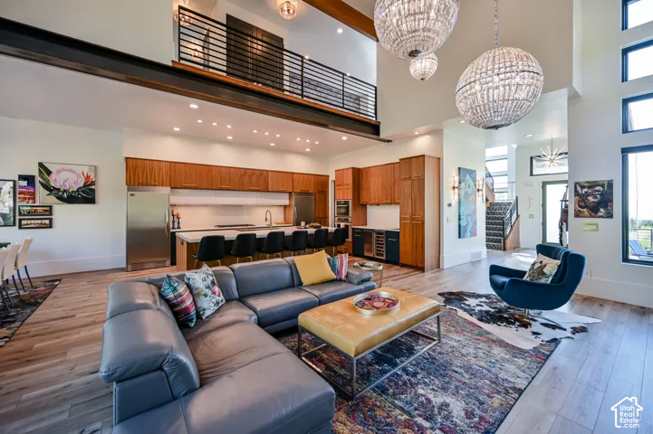 Spacious open-concept living area featuring a double-height ceiling, wood-finish flooring, a contemporary kitchen with a large island, and a prominent second-story balcony with industrial-style railings