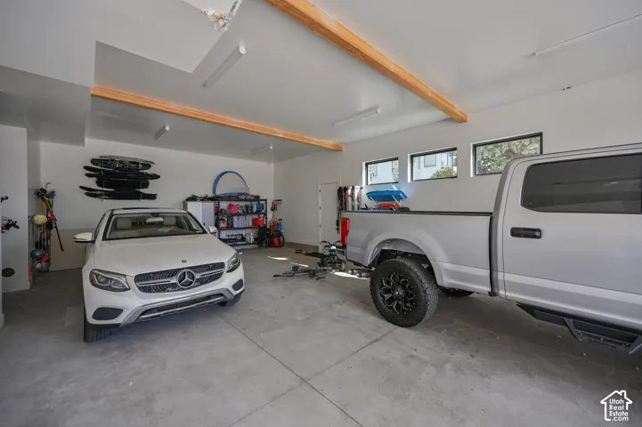 Spacious two-car garage featuring a concrete floor, white walls, exposed wood beams, and multiple windows providing natural light