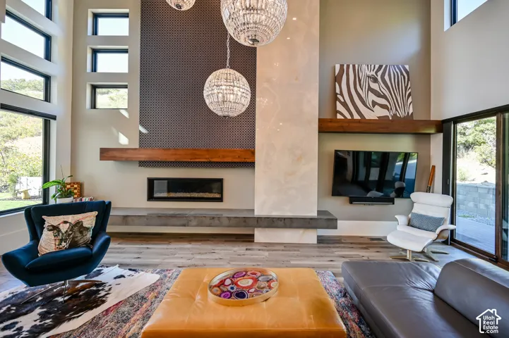 Double-height living space featuring a linear fireplace, decorative patterned wall paneling, a substantial wood mantel, and large picture windows