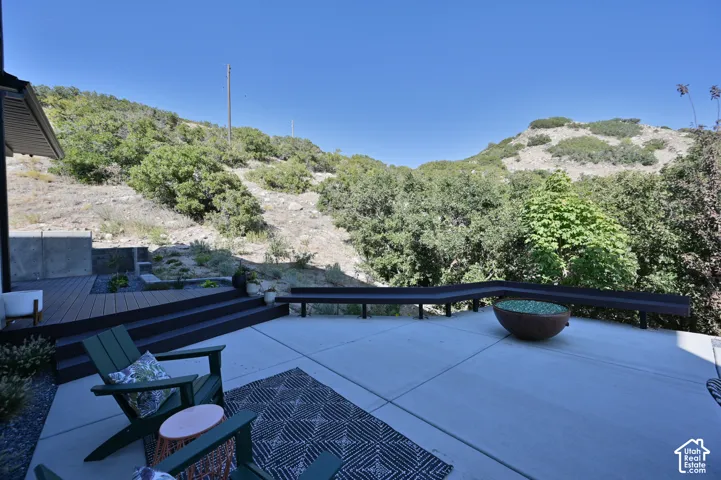 Expansive concrete patio with a tiered composite deck, built-in bench seating, a fire bowl feature, and surrounding mature foliage