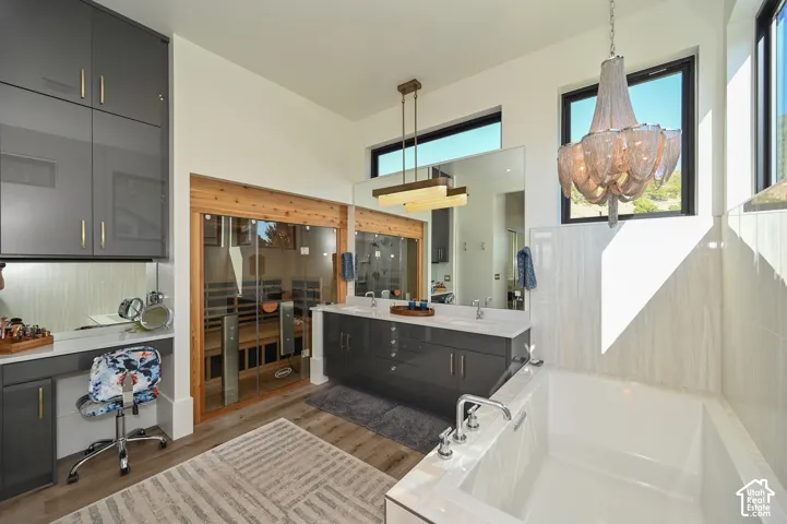 Bathroom featuring a built-in sauna with glass doors, a freestanding soaking tub, dual vanity with quartz countertop, wood-finish flooring, and a makeup vanity with storage