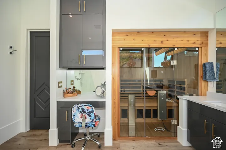Spa-inspired bathroom featuring a glass-enclosed sauna with cedar framing, integrated vanity with quartz countertop, gloss gray cabinetry with brass-finish hardware, and wood-finish flooring