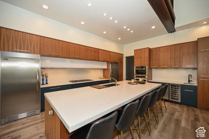 Modern kitchen featuring a large central island with seating, wood-finish flooring, and recessed lighting