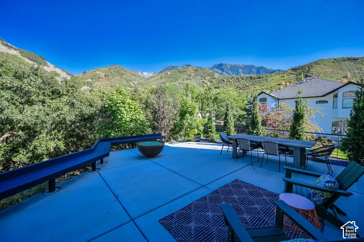 Expansive concrete patio with a modern railing system, a built-in fire pit, and a prominent mountain backdrop