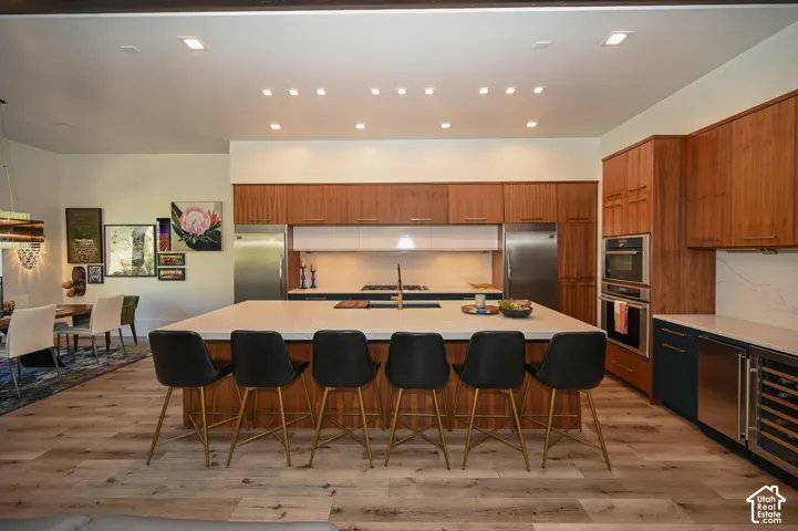 Expansive kitchen featuring a large central island with seating, wood-finish cabinetry, integrated stainless steel appliances, and wood-finish flooring