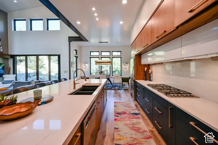 Spacious open-concept kitchen featuring a large island with an integrated sink, quartz countertops, wood-finish flooring, a built-in gas cooktop, and abundant cabinetry