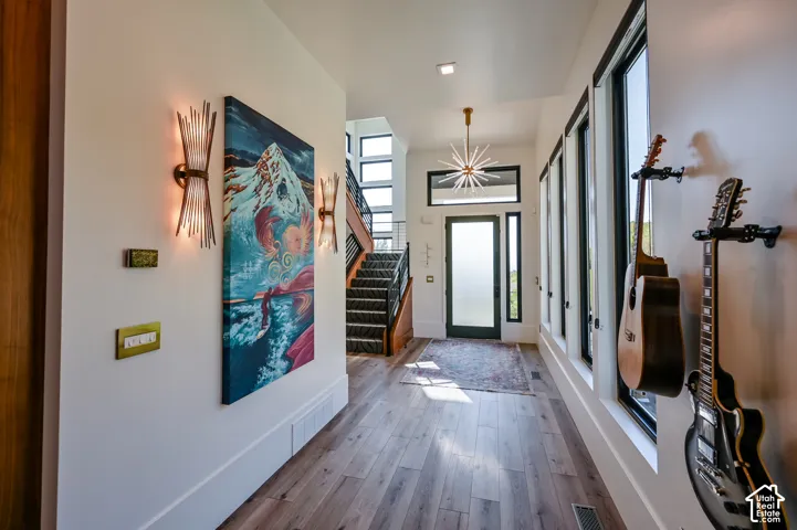 Open-concept entryway featuring wood-finish flooring, a contemporary chandelier, multiple vertical windows with dark trim, a prominent staircase with dark risers, and modern wall sconces