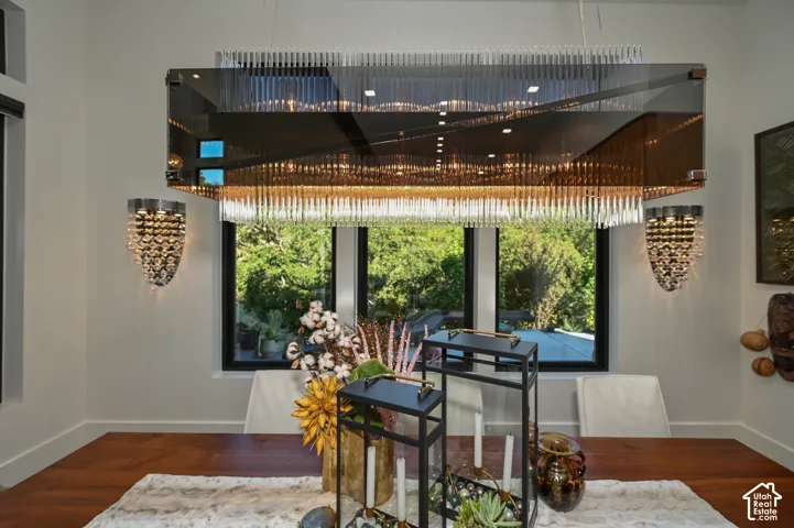 Contemporary dining area featuring a distinctive rectangular chandelier with glass rods, wood-finish flooring, and crisp white walls
