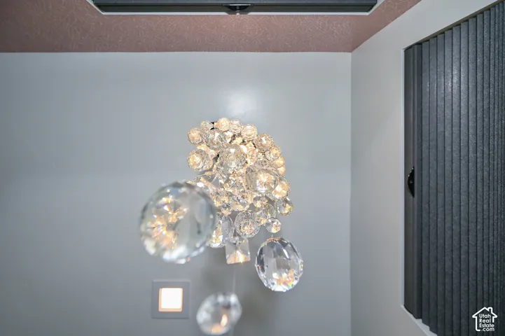 Crystal chandelier with a square recessed light fixture, textured ceiling, and vertical blinds