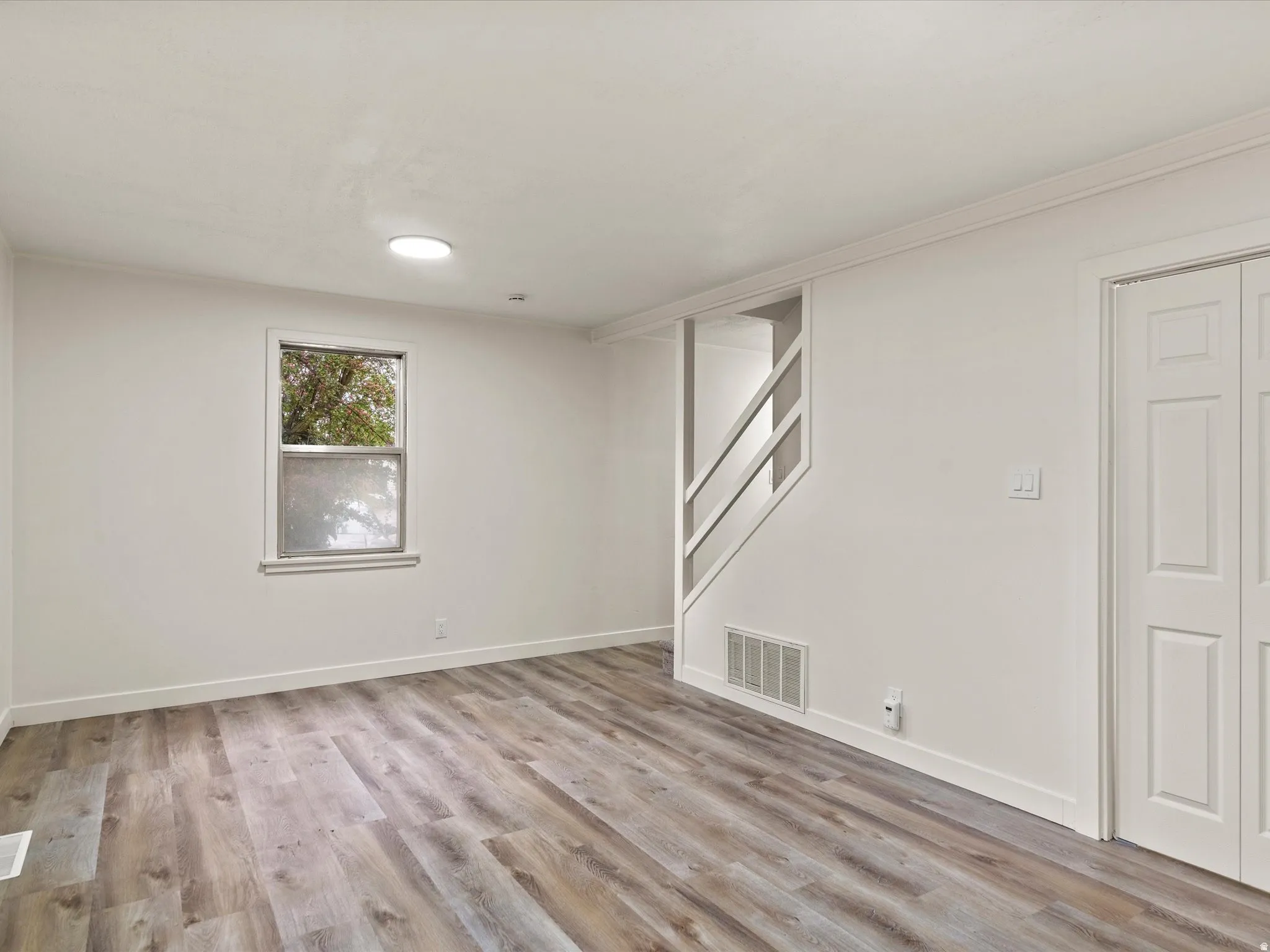 Spacious room featuring wood-finish flooring, white walls, and a single window