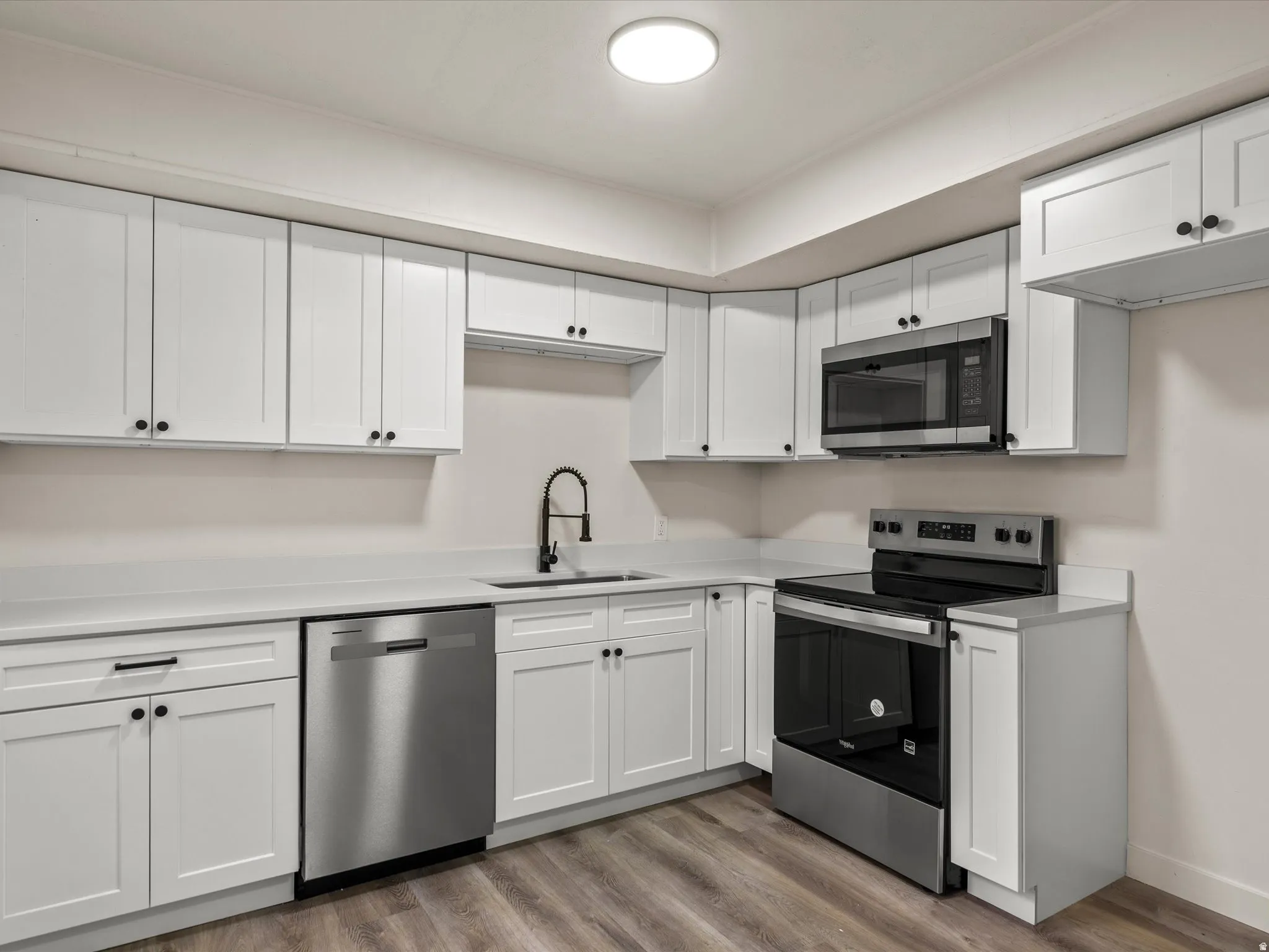 Modern kitchen featuring white shaker cabinetry, stainless steel appliances, light countertops, a matte black faucet, and wood-finish flooring