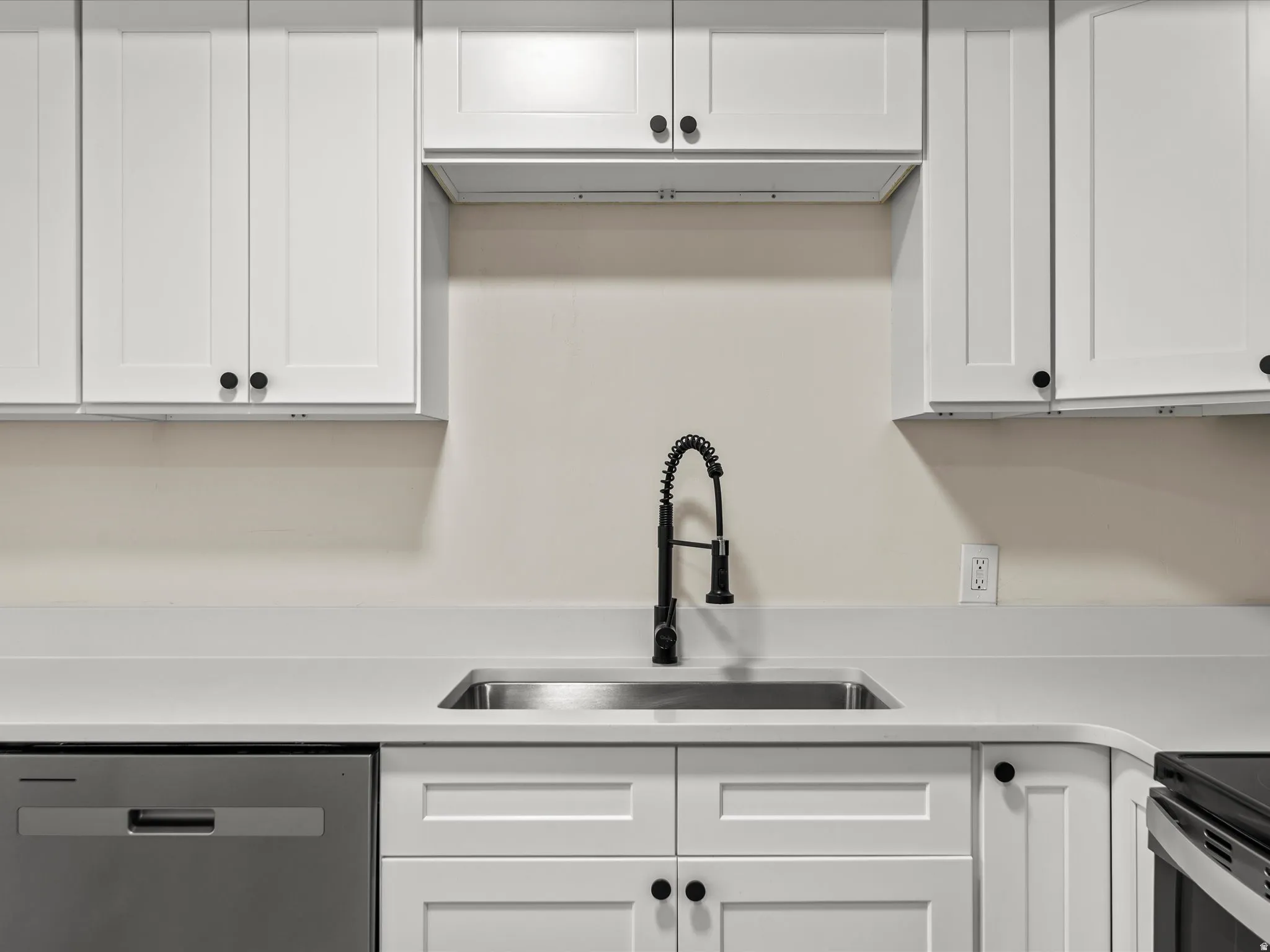 Kitchen featuring shaker-style white cabinetry, light-toned countertops, a stainless steel sink, and a matte black pull-down faucet