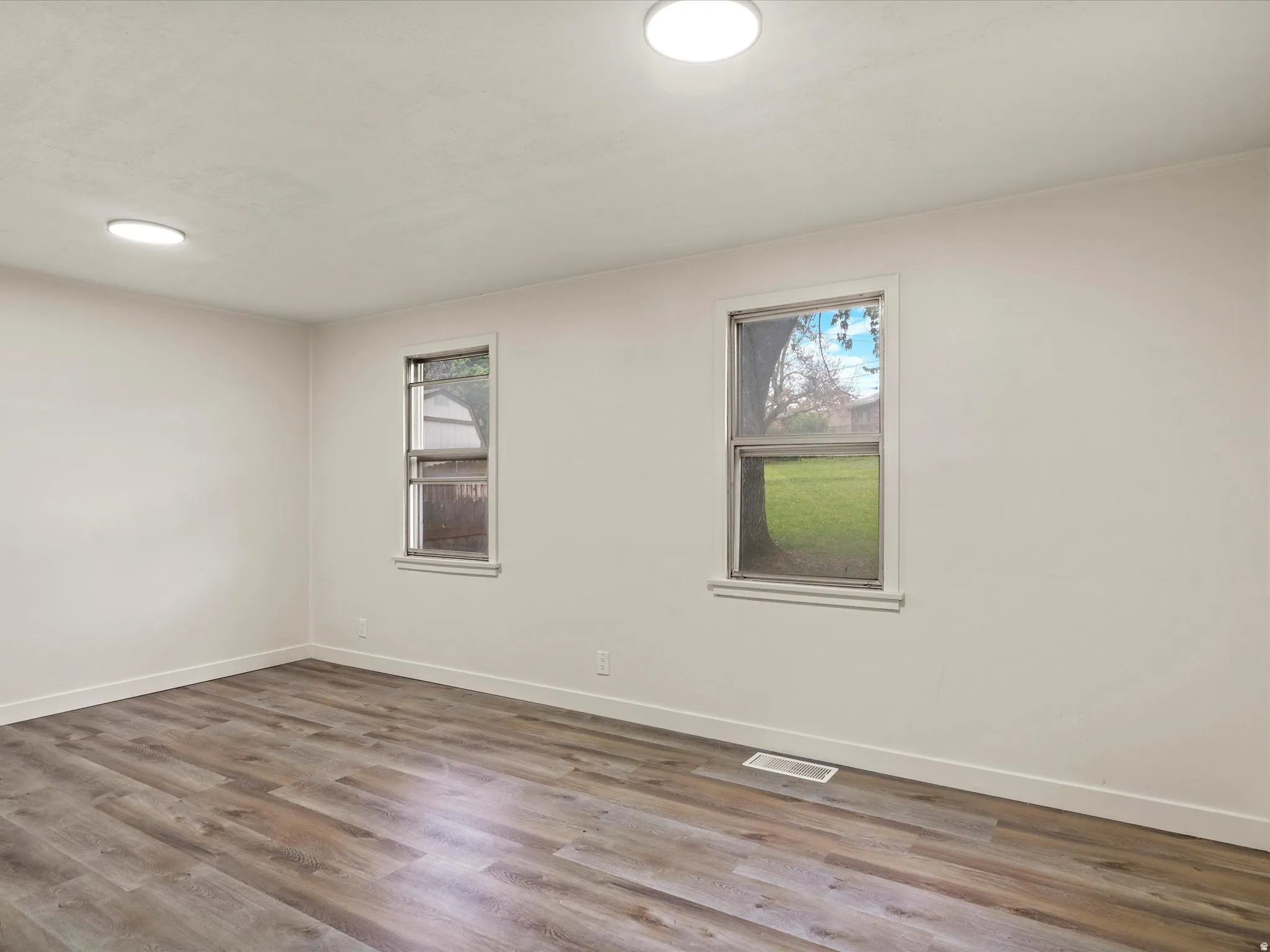 Spacious interior featuring wood-finish flooring, two windows, two flush-mount ceiling lights, and white baseboards