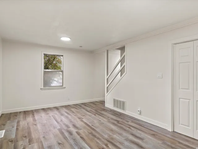 Spacious room featuring wood-finish flooring, white walls, and a single window
