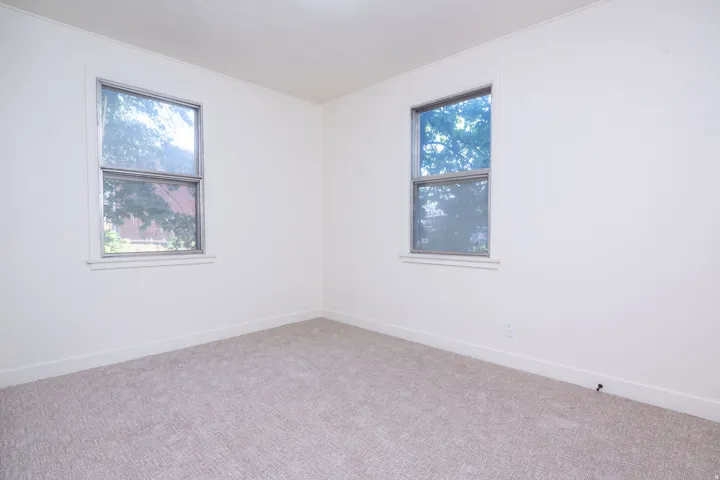 Bright corner bedroom featuring dual windows with natural light, neutral wall finishes, and neutral carpet flooring