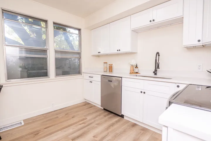 Kitchen featuring white cabinetry, light-toned countertops, wood-finish flooring, a stainless steel dishwasher, and a black gooseneck faucet