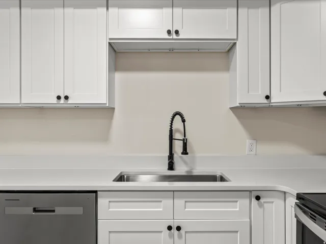 Kitchen featuring shaker-style white cabinetry, light-toned countertops, a stainless steel sink, and a matte black pull-down faucet