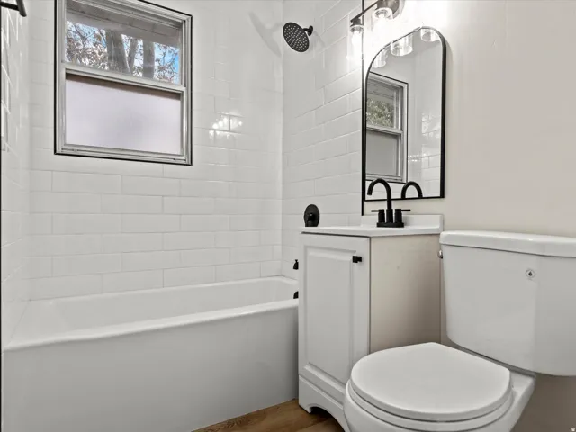 Bathroom featuring a bathtub with subway tile surround, matte black fixtures, wood-finish flooring, a white vanity with integrated sink, and an arched mirror