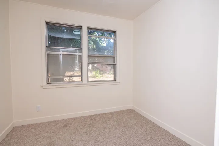 Bright, neutral bedroom featuring dual windows with natural light, neutral carpet flooring, and clean white walls