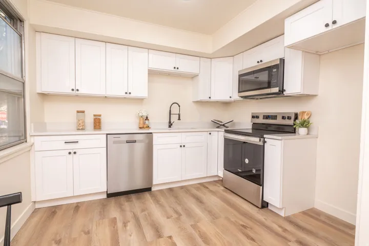 Contemporary kitchen featuring extensive white cabinetry, light-colored countertops, and wood-finish flooring