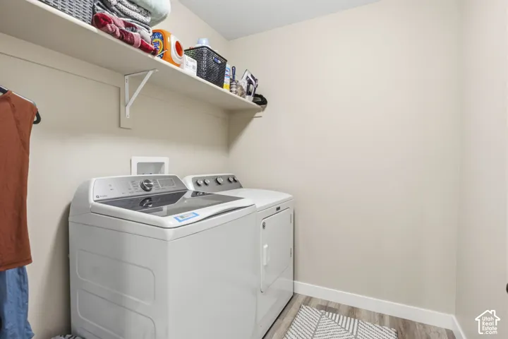 Dedicated laundry area featuring a wall-mounted shelf, light-toned walls, and wood-finish flooring