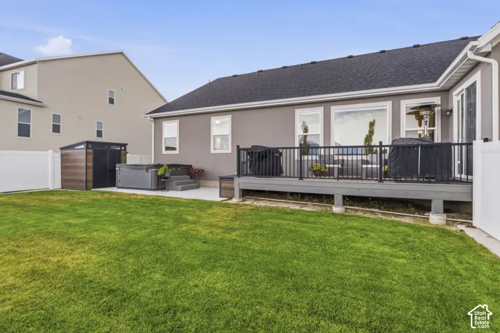 Private backyard featuring a well-maintained lawn, a spacious composite deck with black metal railings, and a concrete patio area with a built-in hot tub