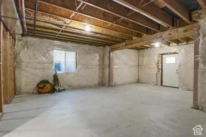 Unfinished basement featuring exposed wood joists, concrete flooring, and insulated walls
