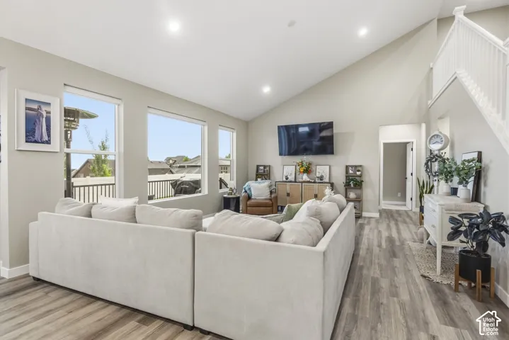 Living area featuring vaulted ceilings, recessed lighting, wood-finish flooring, a white staircase with spindle railing, and multiple large windows