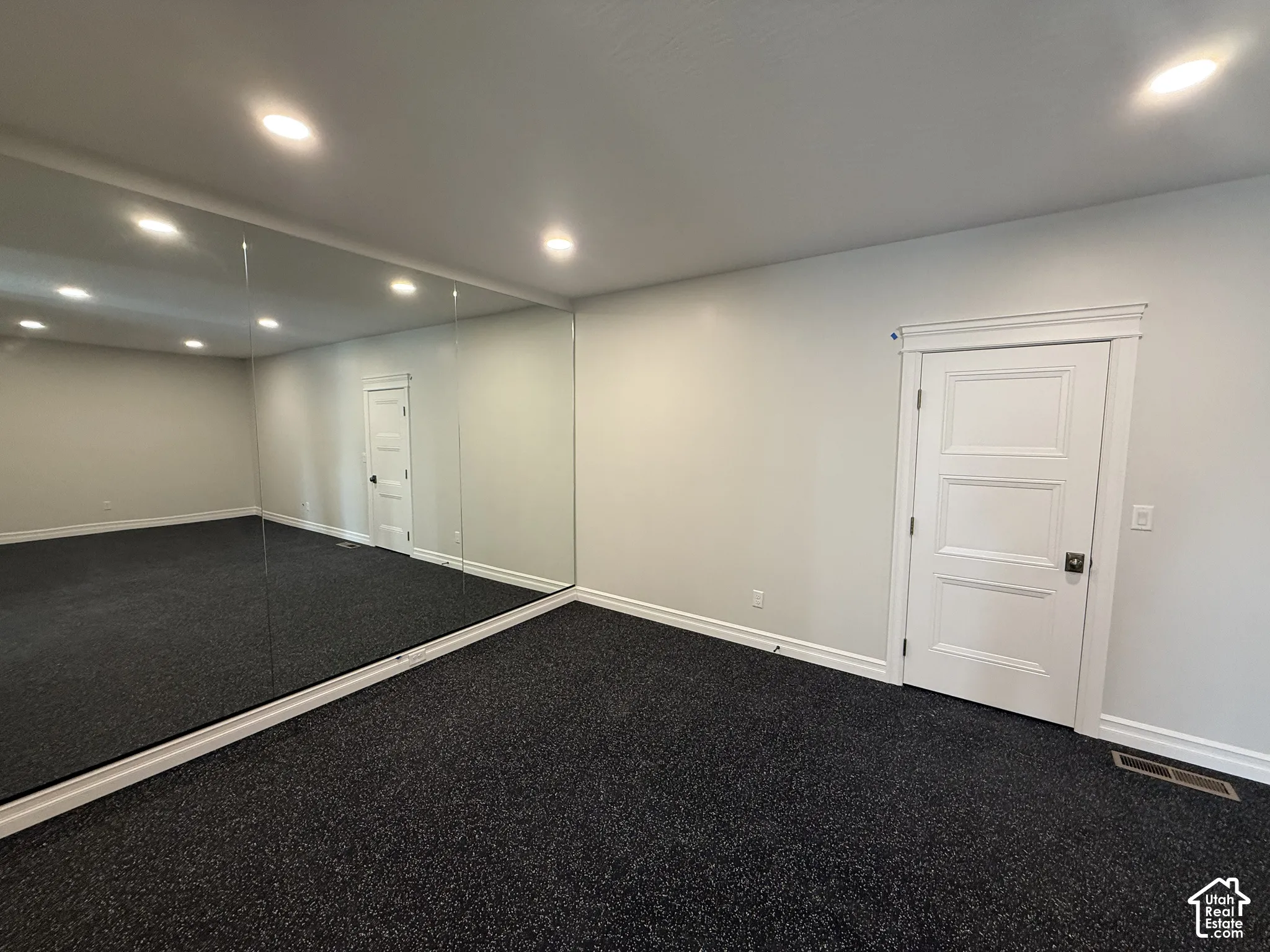 Wall-to-wall mirrored paneling, recessed lighting, neutral wall paint, dark wall-to-wall carpeting, and a classic three-panel interior door with decorative header trim