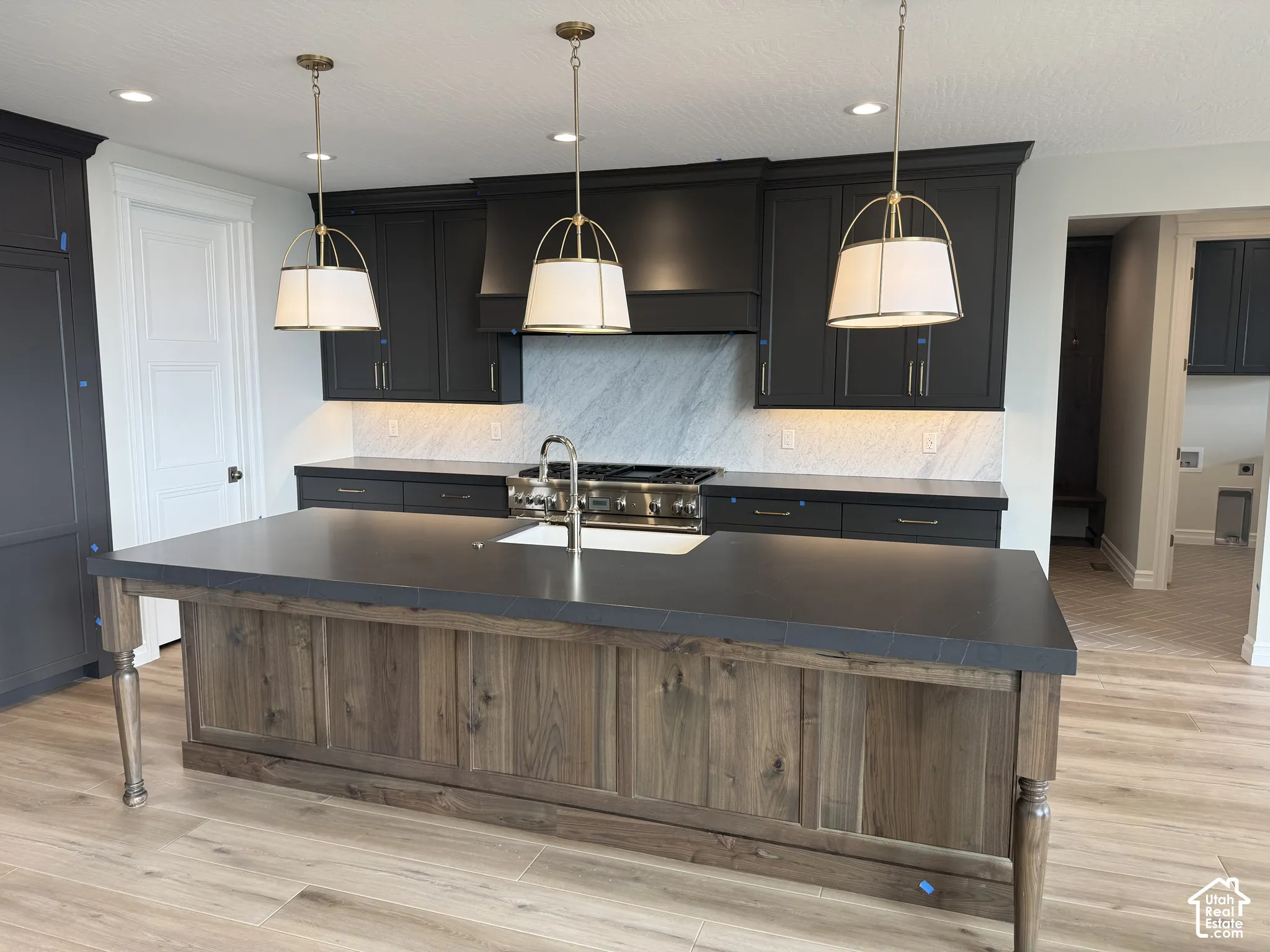 Kitchen featuring a central island with wood-finish paneling, dark stone countertops, custom cabinetry, a stone backsplash, and pendant lighting