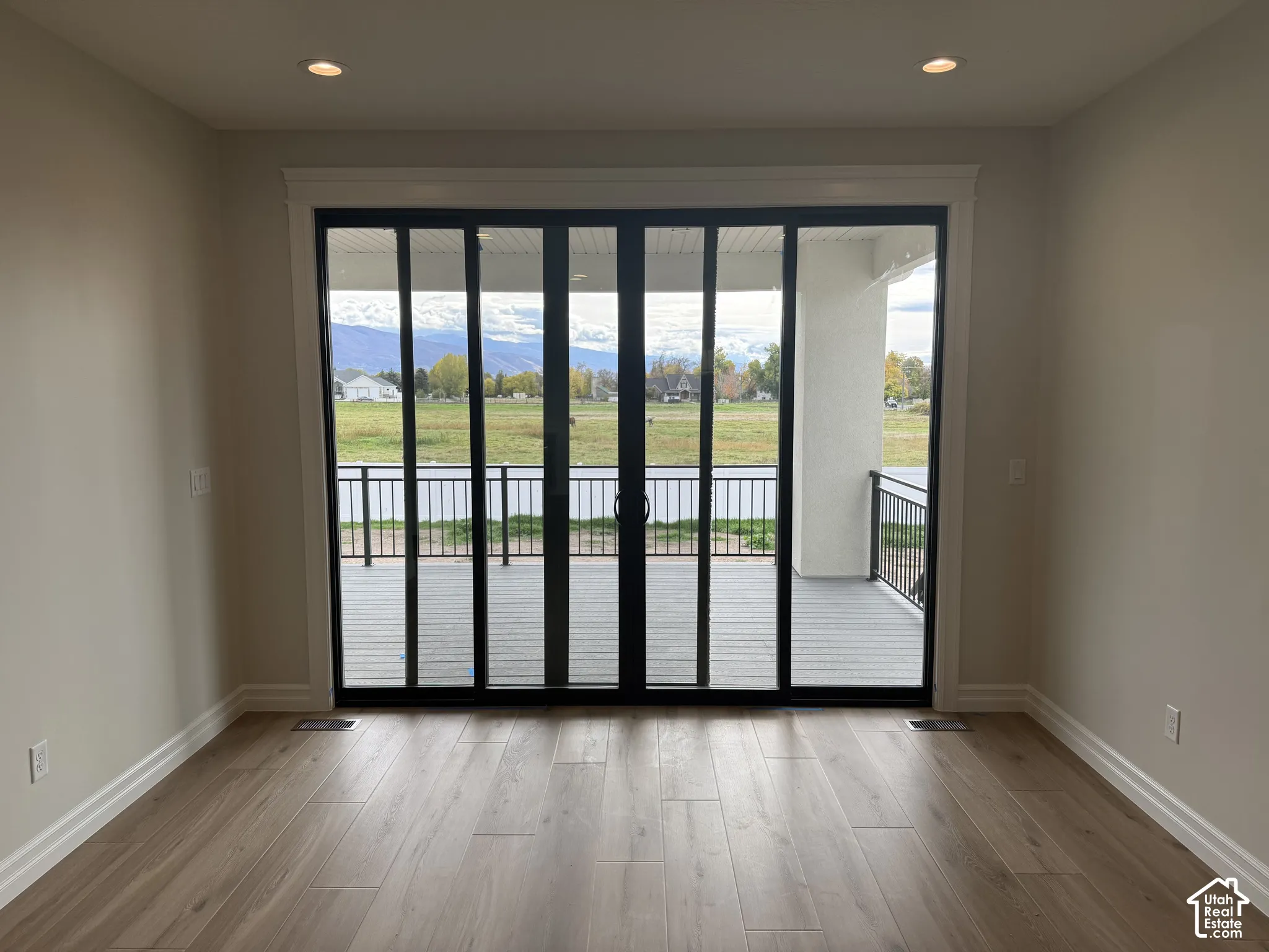 Expansive multi-panel black-framed sliding glass doors featuring wood-finish flooring, recessed lighting, and a covered balcony with metal railing