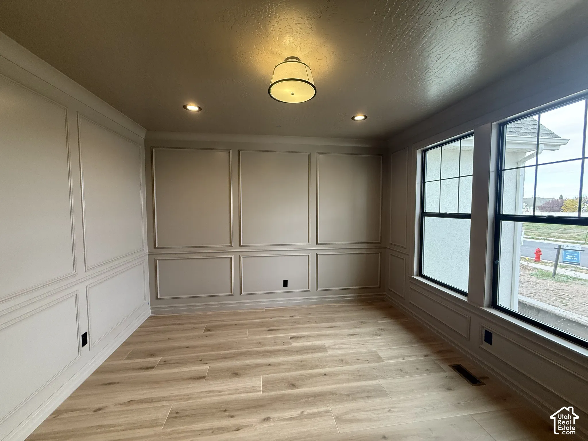 Interior room featuring wainscoting wall paneling, wood-finish flooring, oversized windows with grid detailing, and recessed ceiling lighting with a central drum fixture