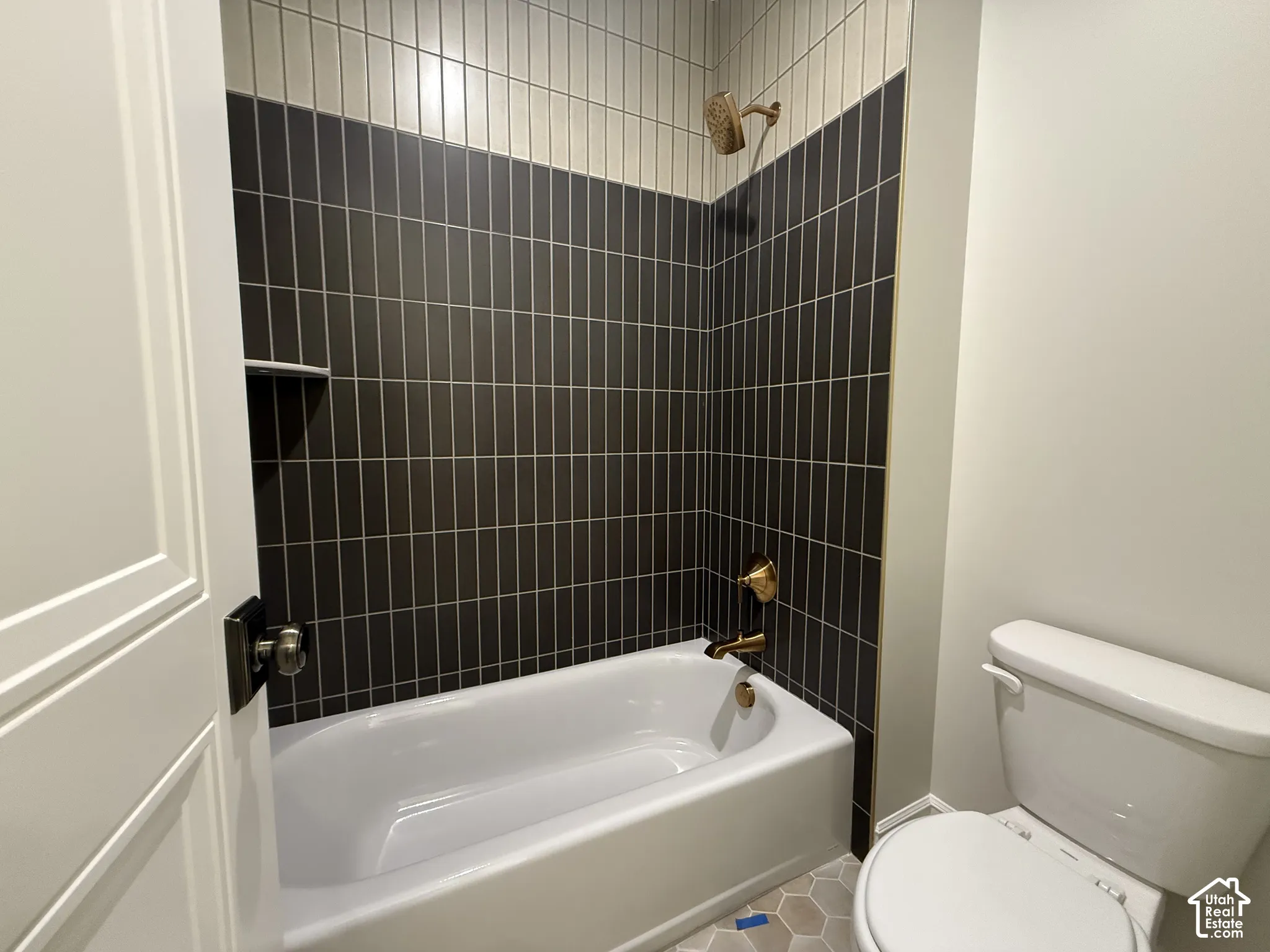 Bathroom featuring a tub-shower combination with floor-to-ceiling vertical tile, hexagonal tile flooring, and metallic finish plumbing fixtures