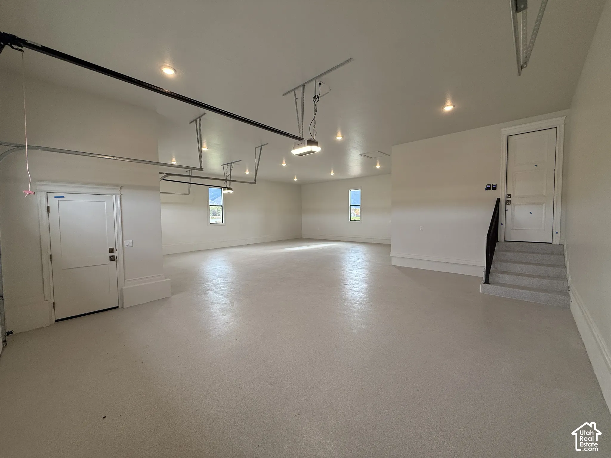 Spacious garage featuring an epoxy-coated concrete floor, recessed lighting, multiple windows, and a dedicated staircase with a metal handrail leading to a separate entry door